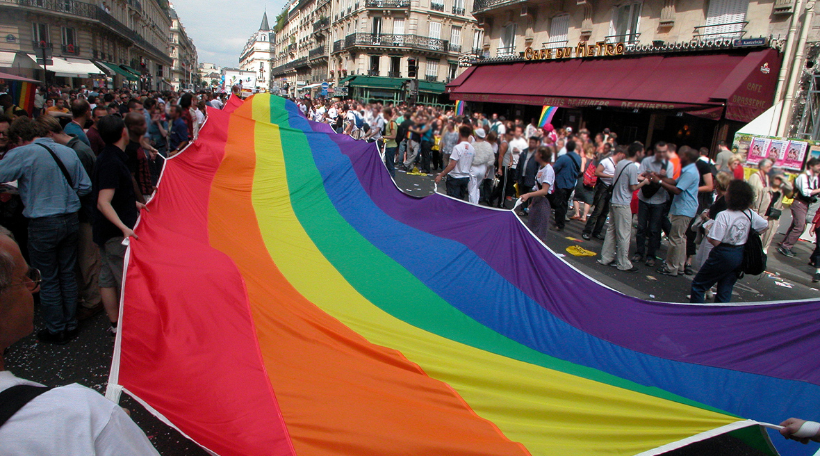 People holding a very big rainbow flag walk through a city street